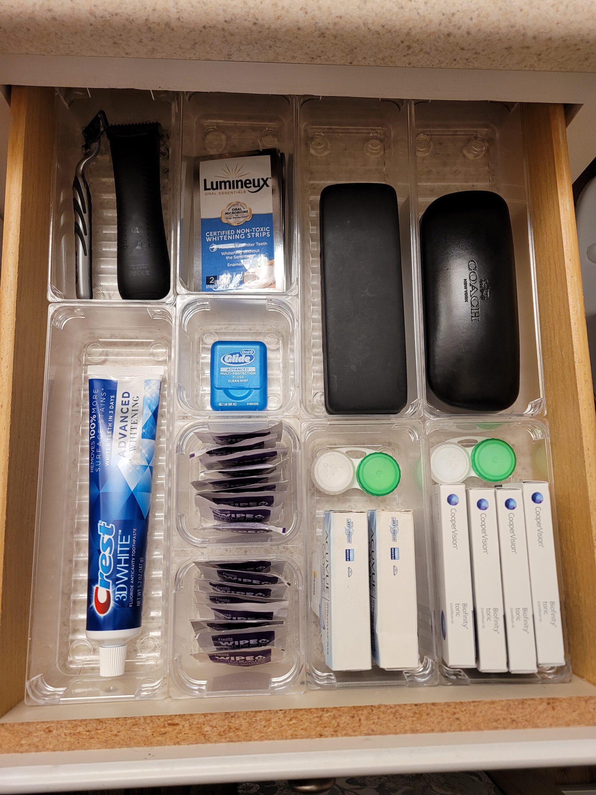 Bathroom drawer with dental, shaving, and vision care categorized into plastic drawer inserts