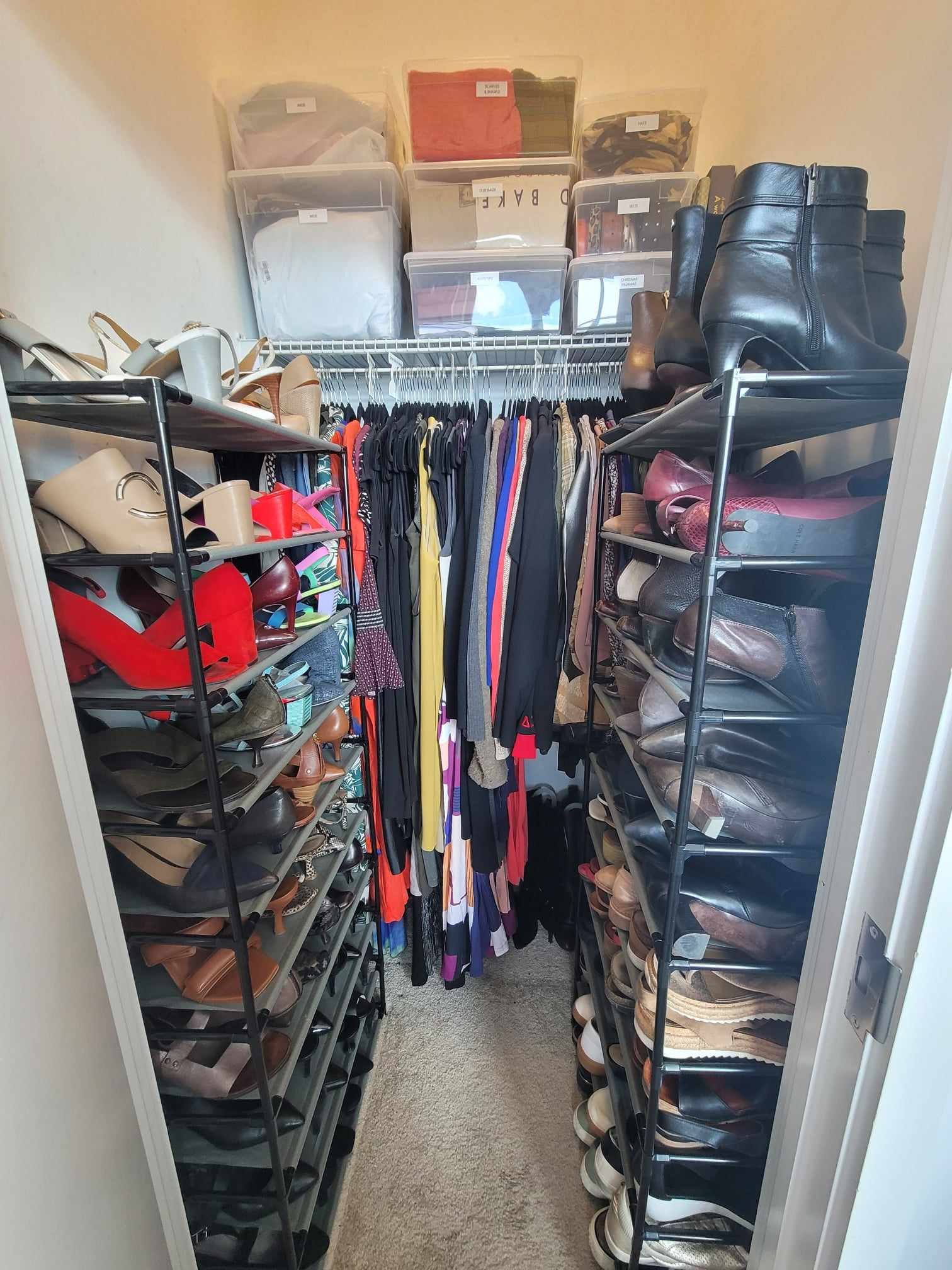 After organization image of primary closet with everything neatly hung, clean floors, accessories binned and labeled, and shoes neatly arranged on shoe racks