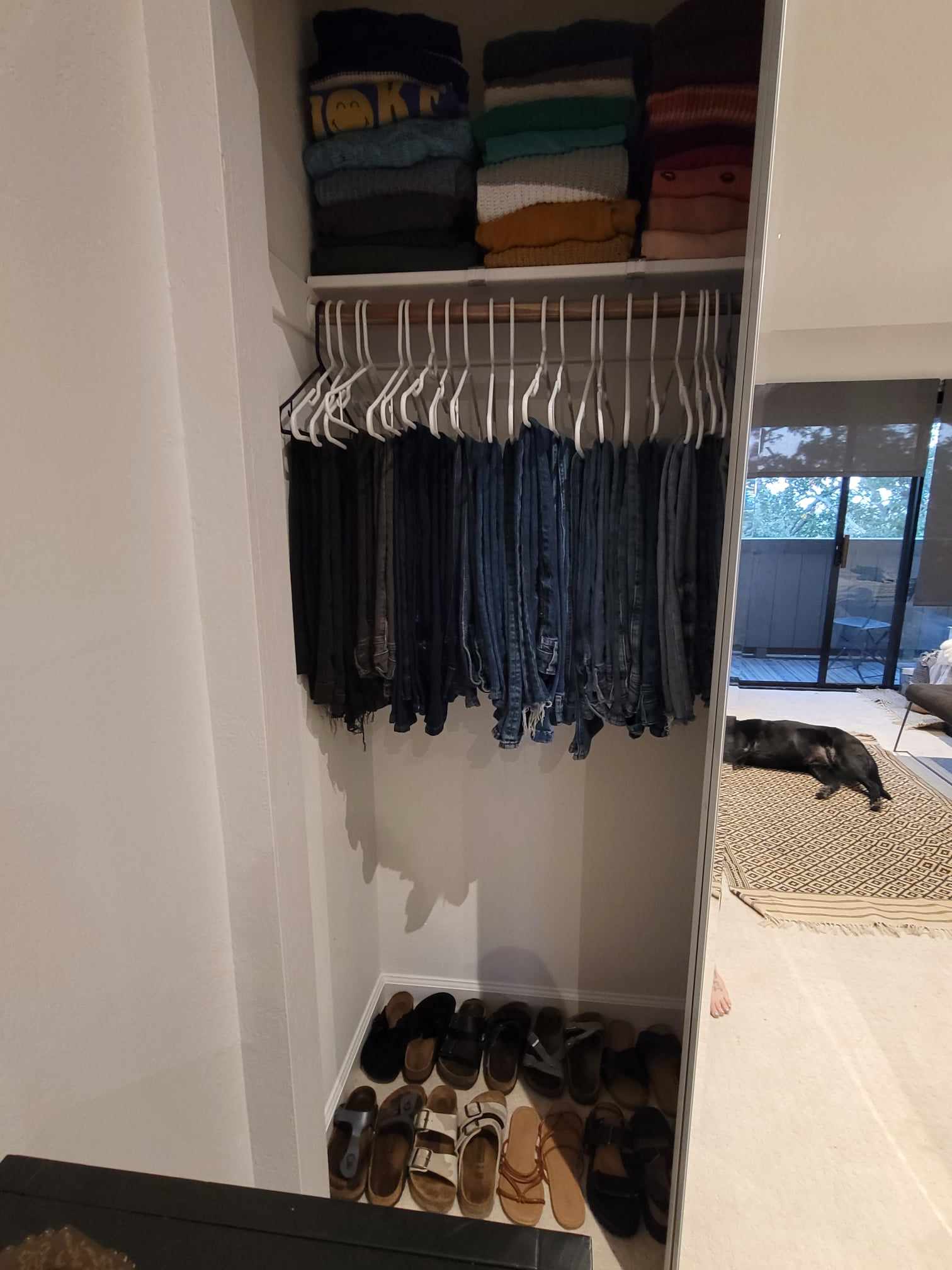 Sweaters neatly folded and jeans neatly hung with shoes organized on the floor of a primary closet