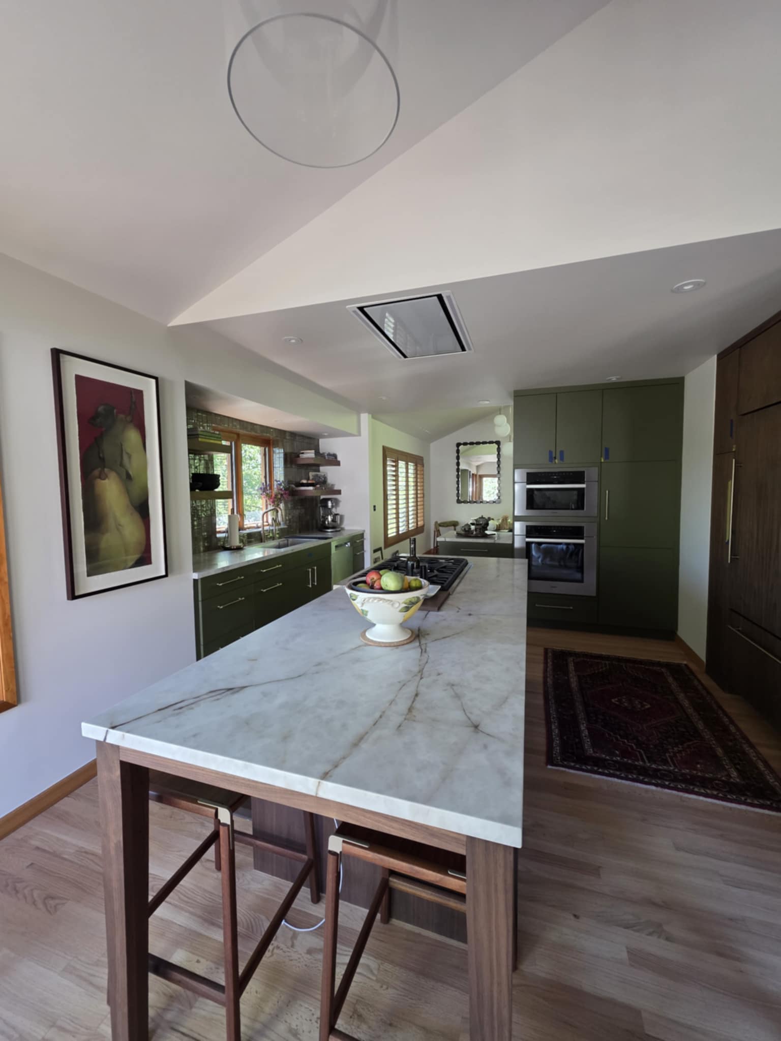 Full view of a kitchen with a marble countertop island and dark green and acacia accents