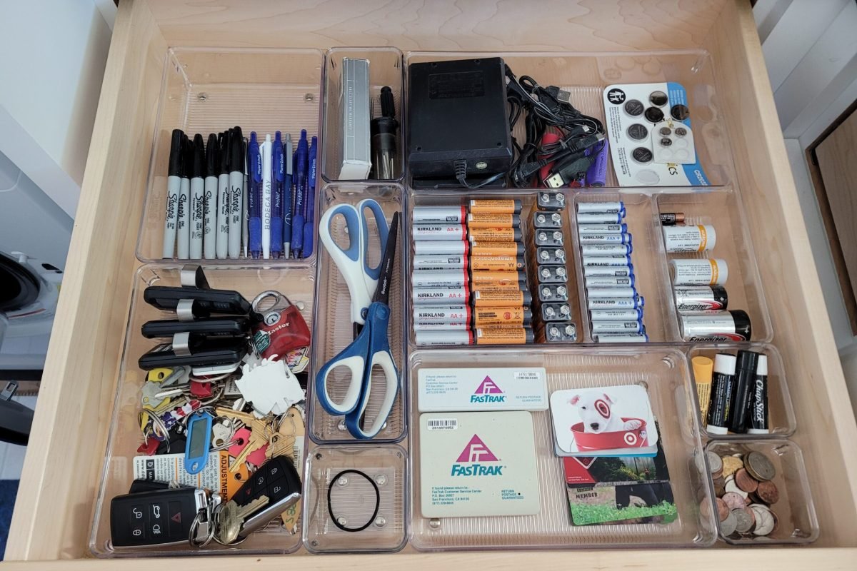 Junk drawer with pens, batteries, keys, change, cards, scissors, and small tools divided with plastic drawer inserts